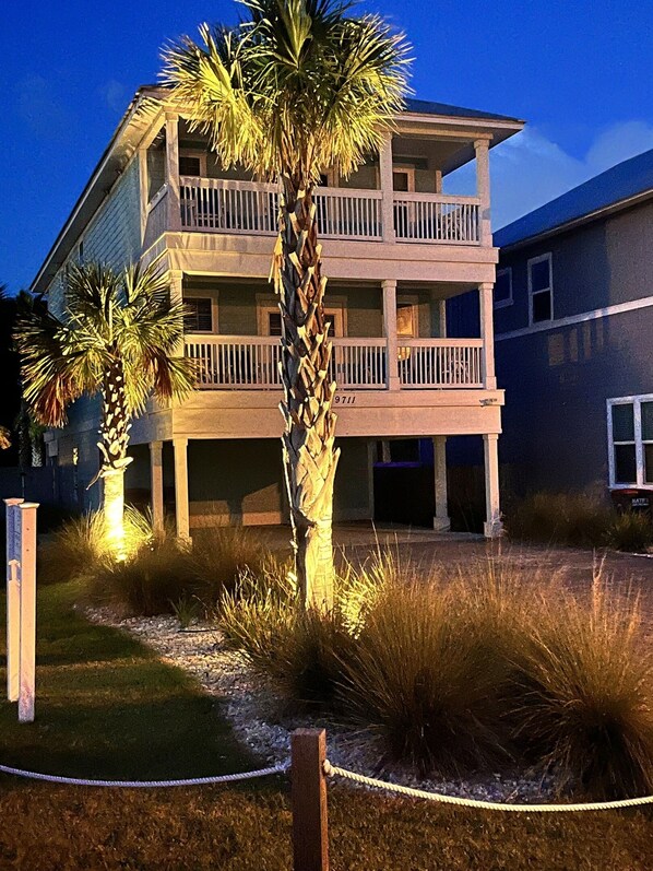 A multi-story building with balconies, surrounded by landscaped areas with palm trees and grasses.