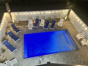 A rectangular pool with lounge chairs and a white fence surrounding it.