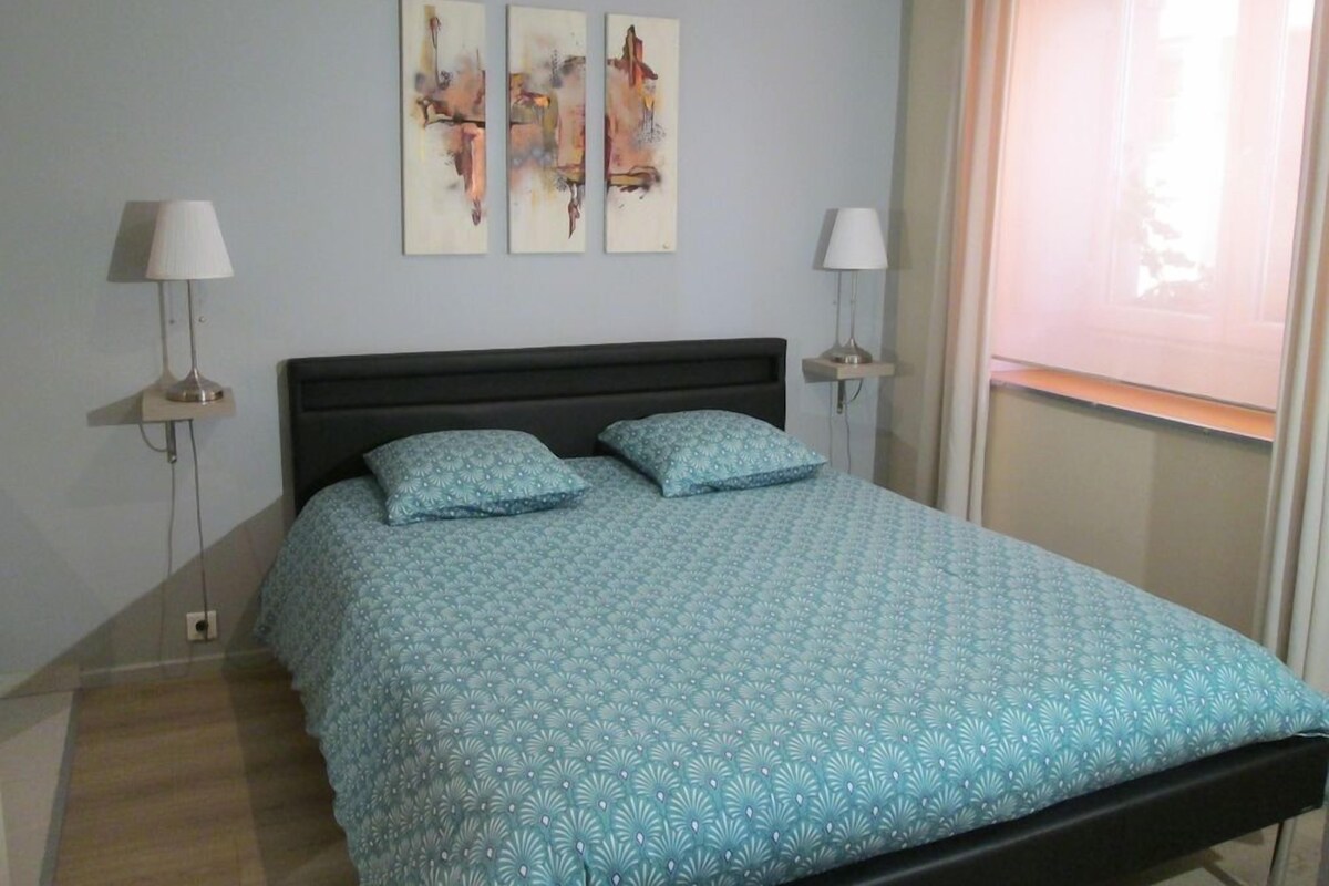 A bedroom with a bed, two wall-mounted lamps, and abstract art on the wall.