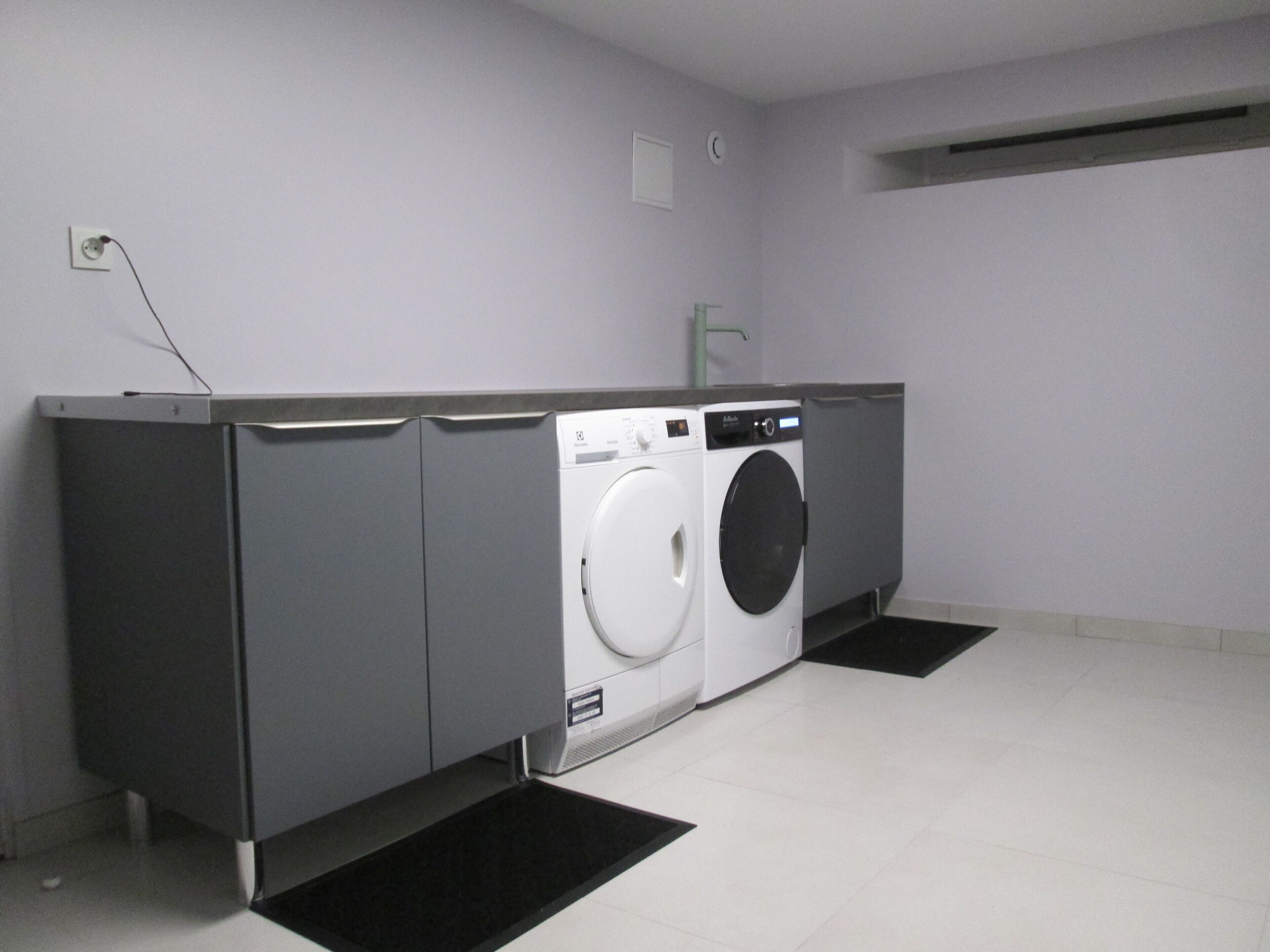 A laundry room with a washing machine and dryer, grey cabinets, and a tiled floor.