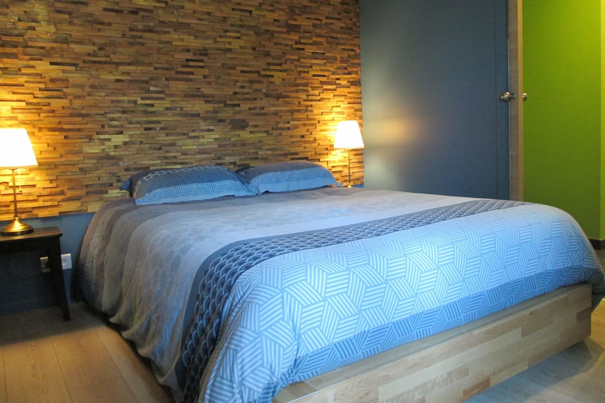 A bedroom with a wooden headboard, a bed with patterned bedding, two bedside lamps, and a green door.