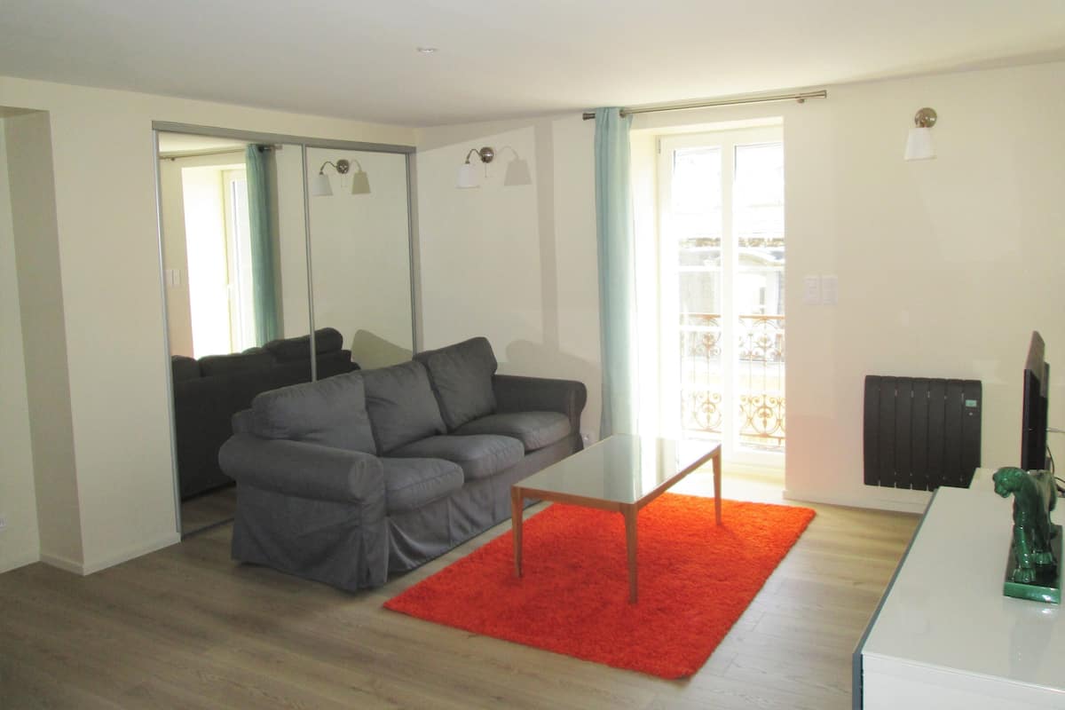 A modern living room with a grey sofa, a small white table, and a red rug.