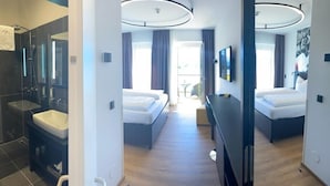 A modern hotel room with a separate bathroom, a bed, a desk, and a view of the outdoors.