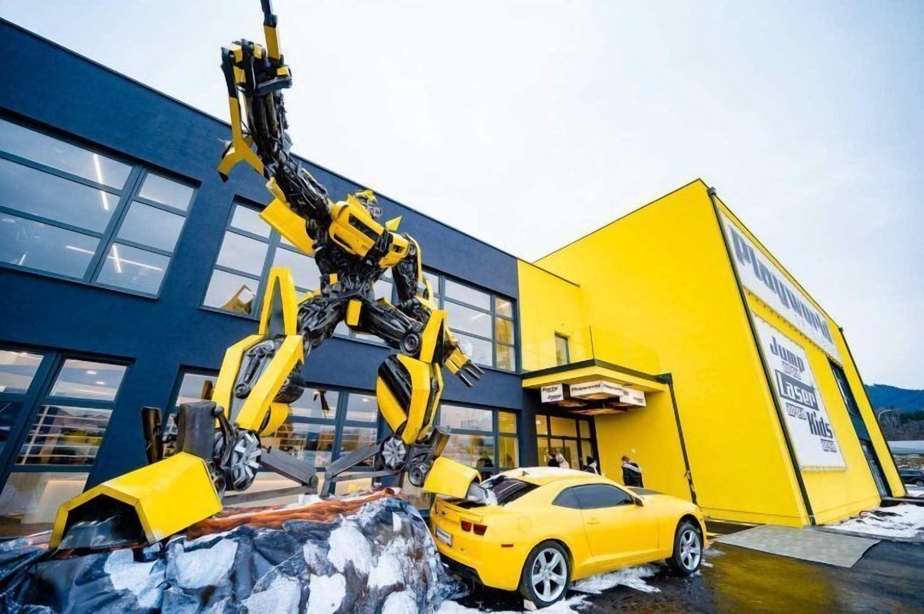 Un auto amarillo estacionado frente a un edificio con una escultura grande, amarilla y negra.
