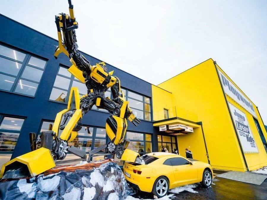 Un auto amarillo estacionado frente a un edificio con una escultura grande, amarilla y negra.