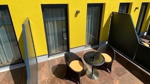 A yellow building with large windows and a patio area with two wicker chairs and a small table.