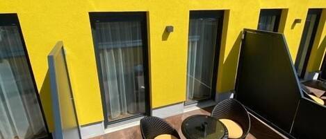 A yellow building with large windows and a patio area with two wicker chairs and a small table.