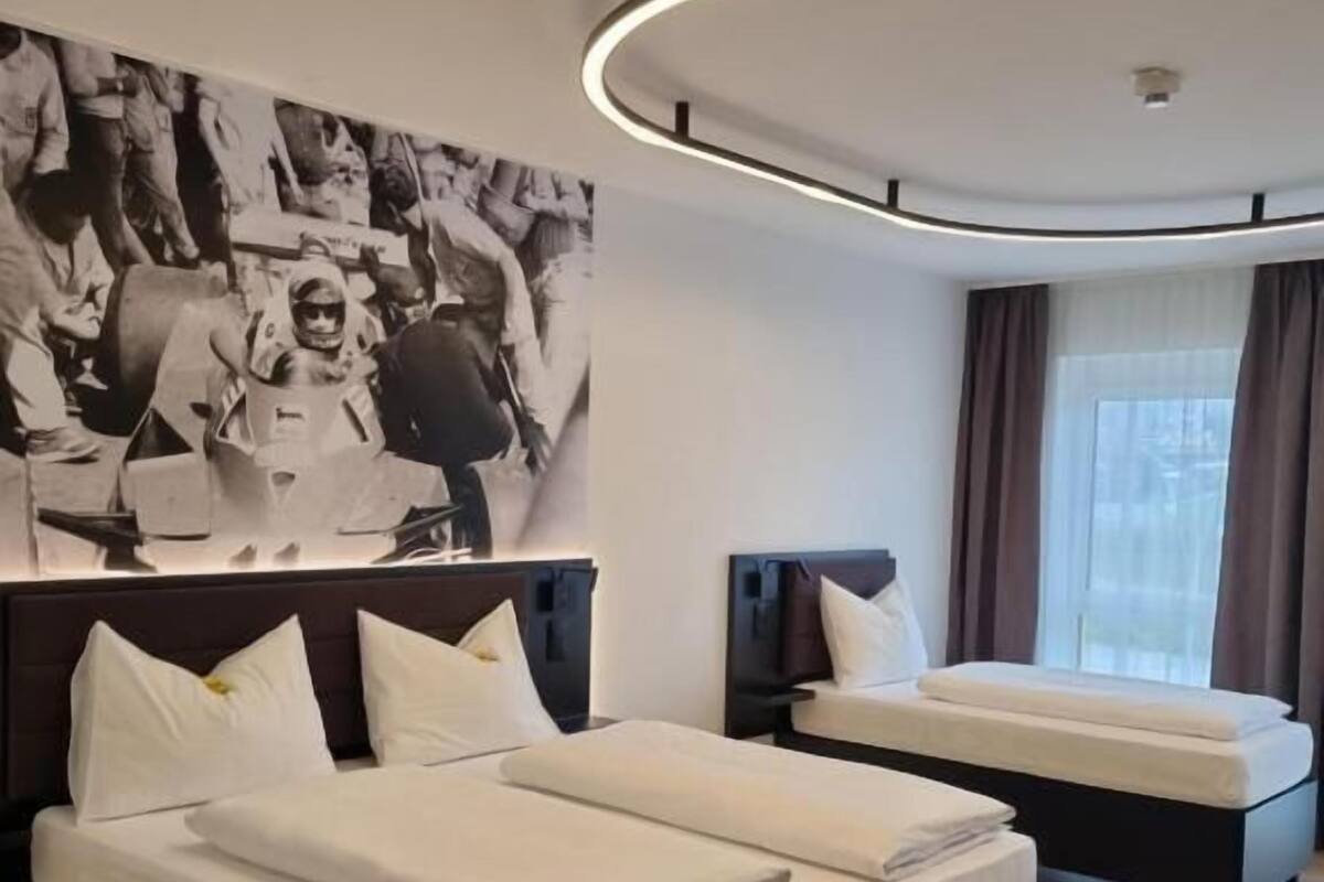 A modern hotel room with a large bed, a smaller bed, a seating area, and a large abstract painting on the wall.