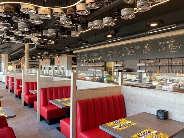 Ein modernes Restaurant mit roten Sitzecken, einer Kreidetafel mit der Speisekarte und einer Auswahl an angebotenen Speisen.