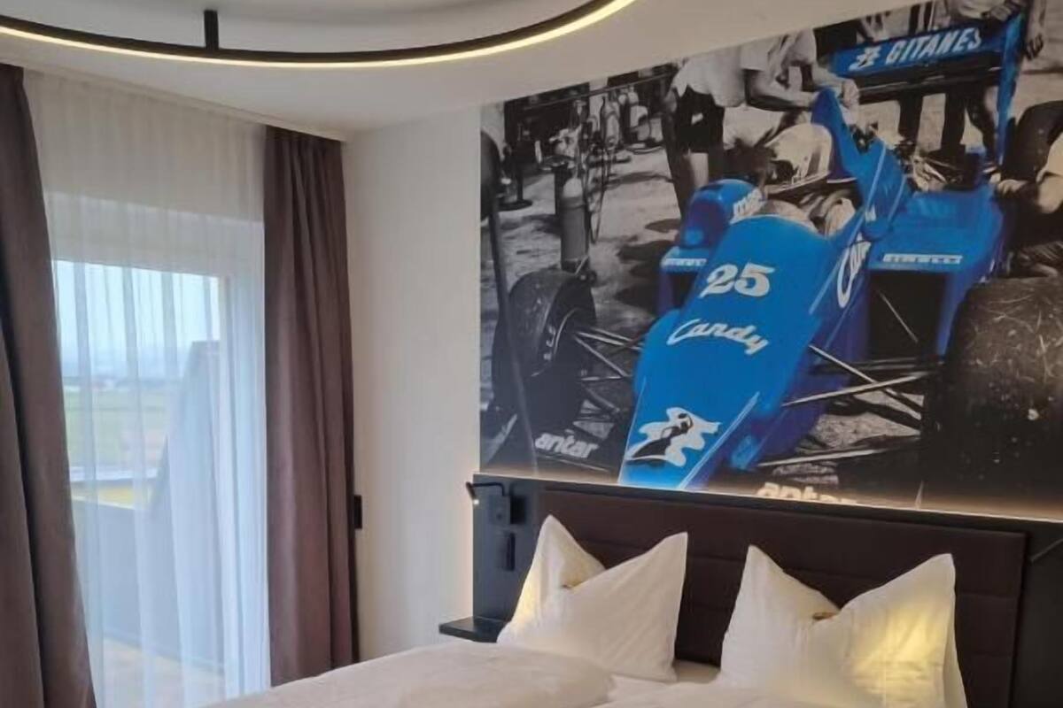 A modern hotel room with a large bed, a headboard with a poster, and a view through the window.
