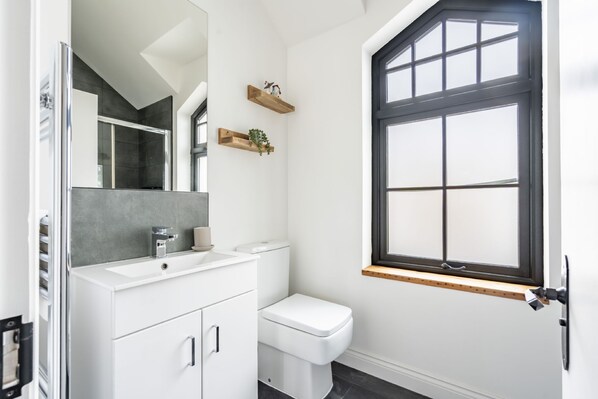 A modern bathroom with a white vanity, a toilet, and a large window with a black frame.