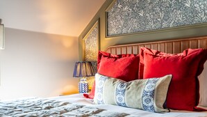Una cama bien hecha con ropa de cama estampada, cabecera con diseño floral y mesita de noche con lámpara y objetos decorativos.