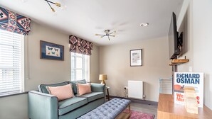 A modern living room with a teal sofa, a wooden bench, a lamp, and a mounted TV. - The Falcon - Apartment 1 (York)