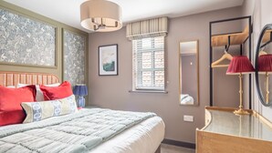 A neatly arranged bedroom with a bed, a bedside table, a mirror, and a window with blinds. - The Falcon - Apartment 1 (York)