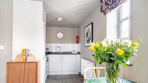 A modern kitchen with white cabinets, a wooden cabinet with books, and a dining area with a table and vase of flowers. - The Falcon - Apartment 1 (York)