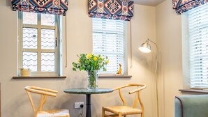 A room with two wooden chairs, a small round table with a vase of yellow flowers, and a floor lamp. - The Falcon - Apartment 1 (York)