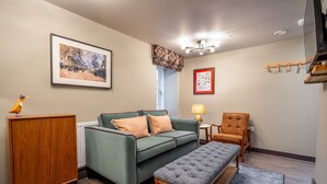 A living room with a green sofa, a wooden cabinet, a bench, a red rug, a lamp, and a framed picture on the wall. - The Falcon Apartment 5 (York)