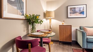 A dining area with a table set for two, a vase with flowers, a lamp, and a framed painting on the wall. - The Falcon Apartment 5 (York)