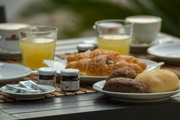 A breakfast table with croissants, muffins, and a plate of butter packets.