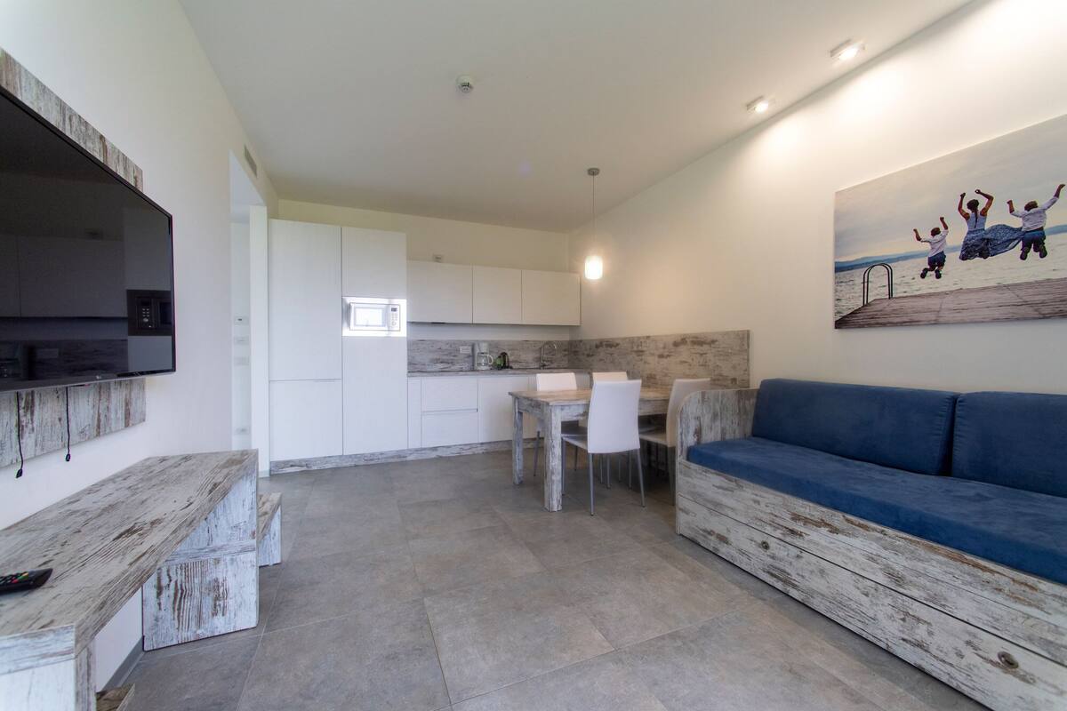 Un espacio habitable compacto con kitchenette, comedor y zona de estar con un sofá azul.