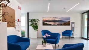 Un moderno vestíbulo de hotel con tres sillones azules, una mesa de centro blanca, un cuadro de paisaje grande y una planta en maceta.