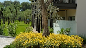 Un edificio moderno con un árbol en primer plano y un jardín lleno de flores amarillas.