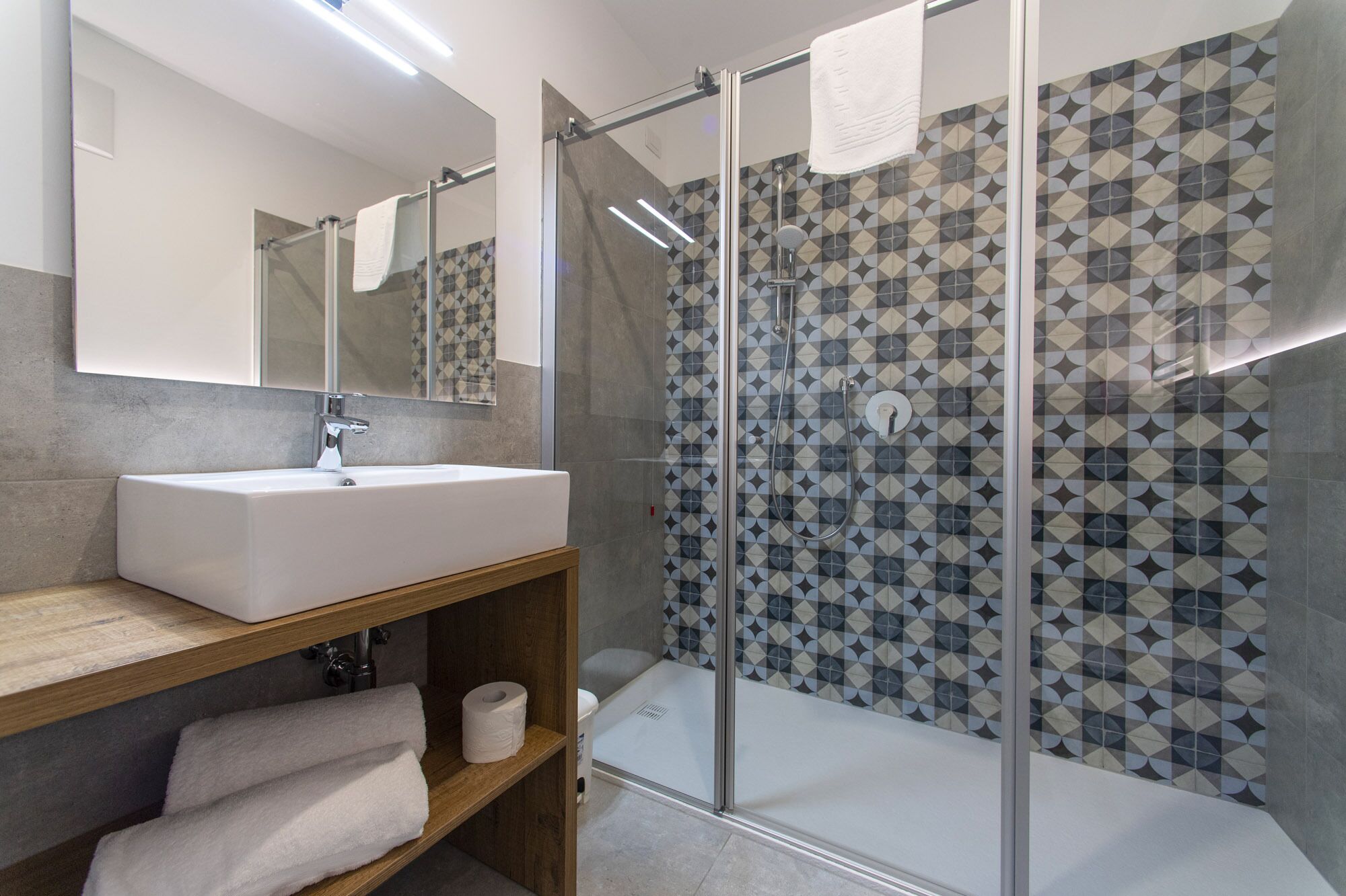 A modern bathroom with a glass-enclosed shower, a white sink, and a patterned tile wall.