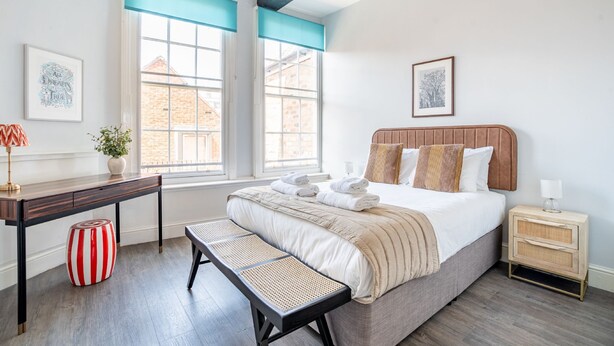 Une chambre à coucher comprenant un lit, des tables de chevet, un bureau, un banc et de grandes fenêtres.