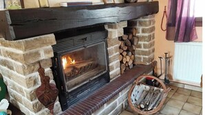 A stone fireplace with a black mantel, a fire burning inside, and a basket of firewood to the right. - La Poulette (Ancy-le-Libre)