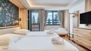 A hotel room with two beds, a TV, a wooden dresser, and a balcony with a view of trees and mountains. - Chalet Hôtel Turquoise (La Plagne-Tarentaise)