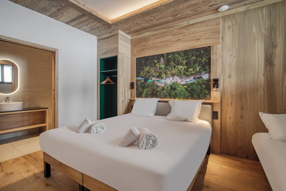 Un dormitorio moderno con una cama grande, cabecera de madera y un cuadro de un paisaje boscoso.