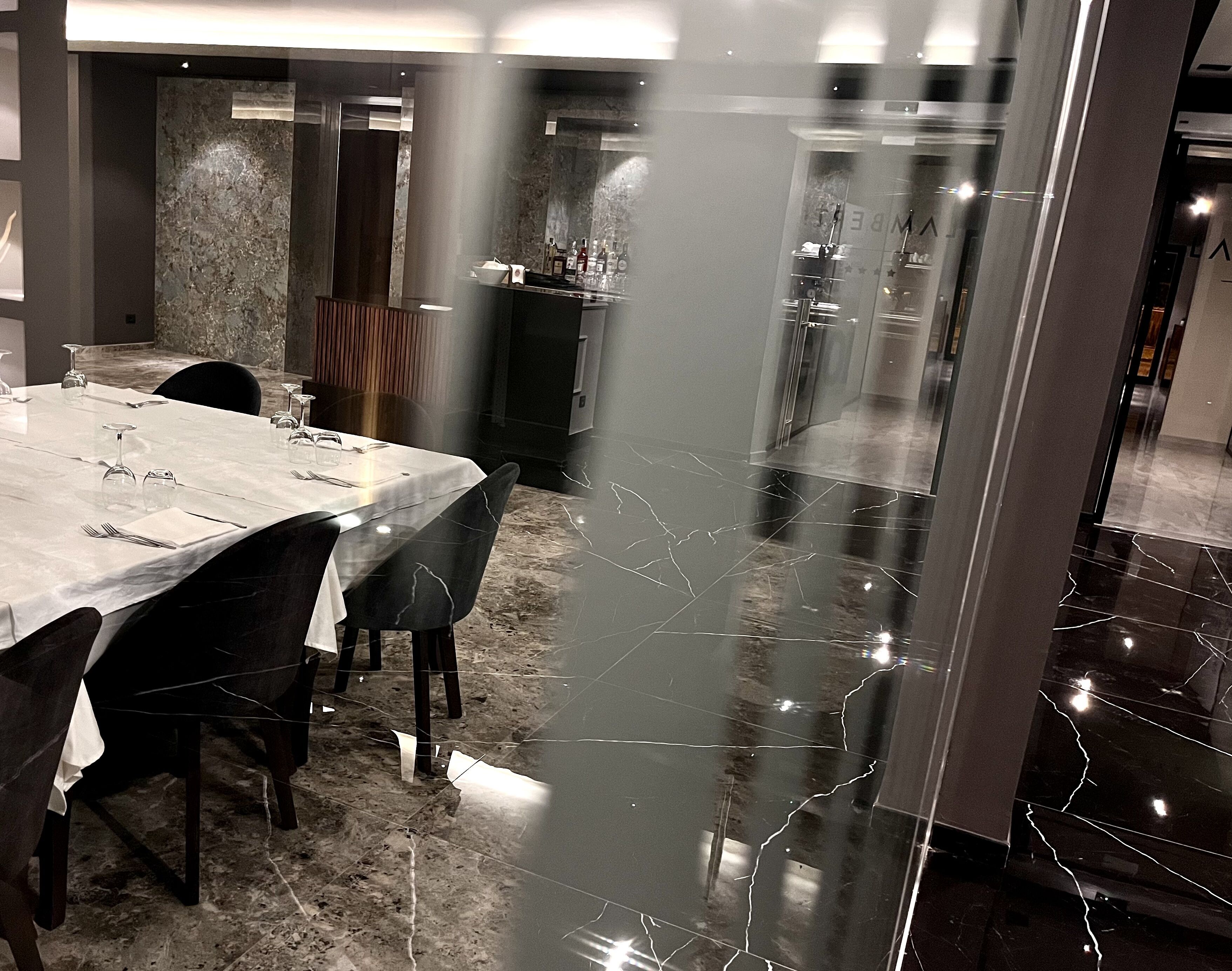 Un comedor con piso de mármol, un separador de vidrio y una mesa lista para servir.