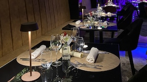 A restaurant with tables set for dining, a view of the night sky, and indoor lighting.