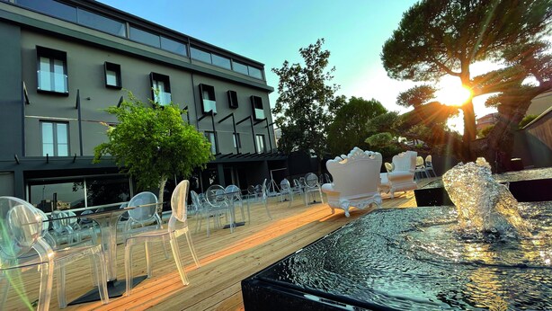 A modern hotel exterior with a wooden deck, clear chairs, and a fountain.