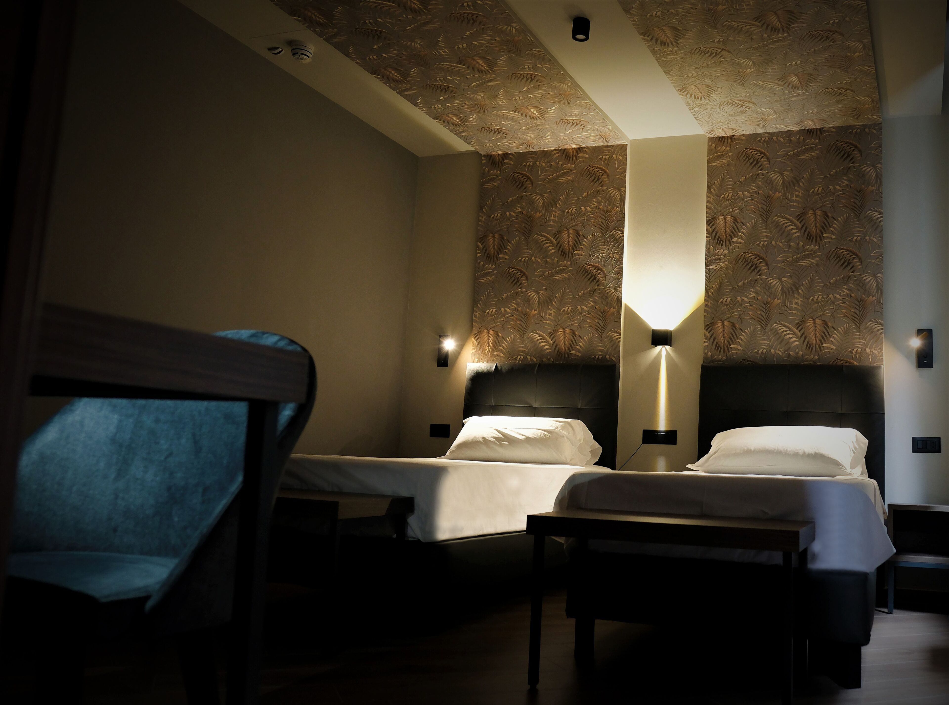 Une chambre d’hôtel avec deux lits, une table de chevet, une chaise et un mur décoré d’un motif.