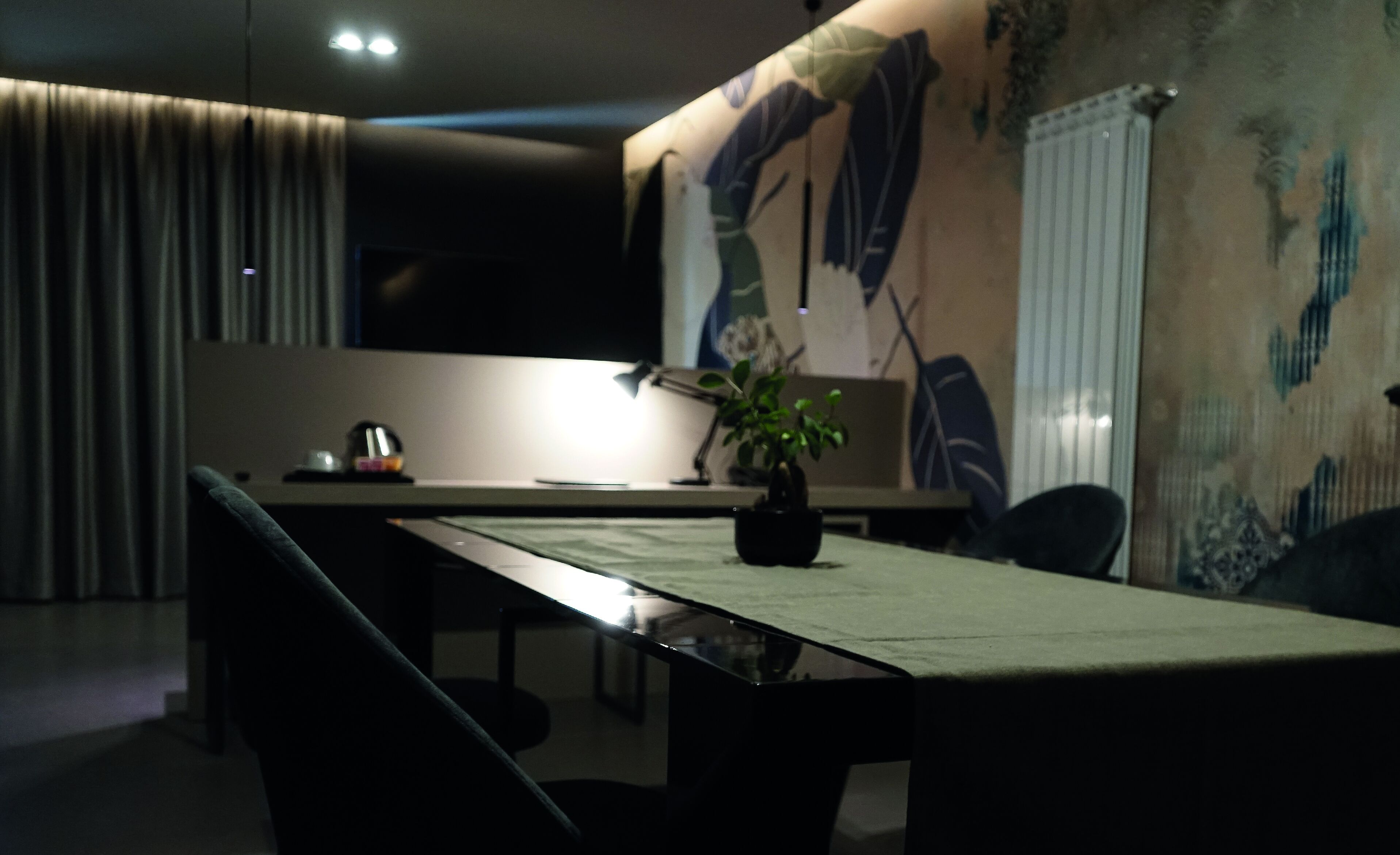 Un comedor moderno con una mesa larga, sillas, una planta en maceta y una pared con estampado floral.