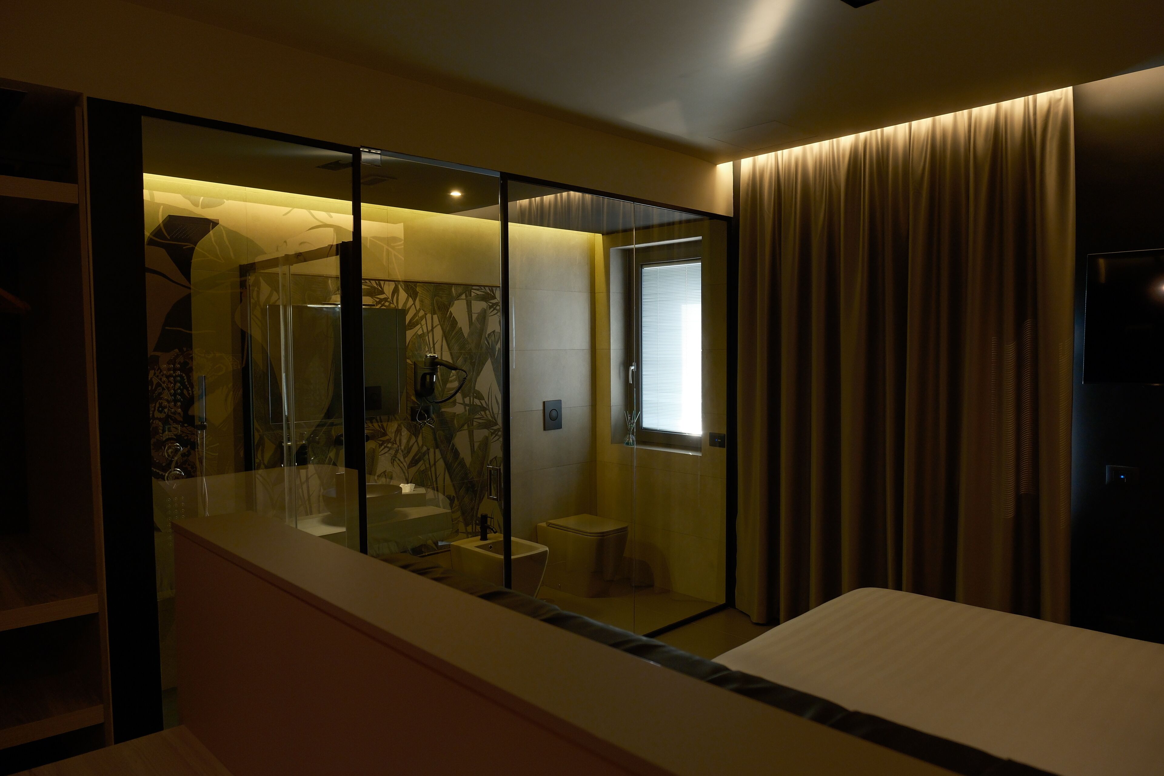 A modern hotel room with a glass-enclosed shower, a small bathroom, and a bed.