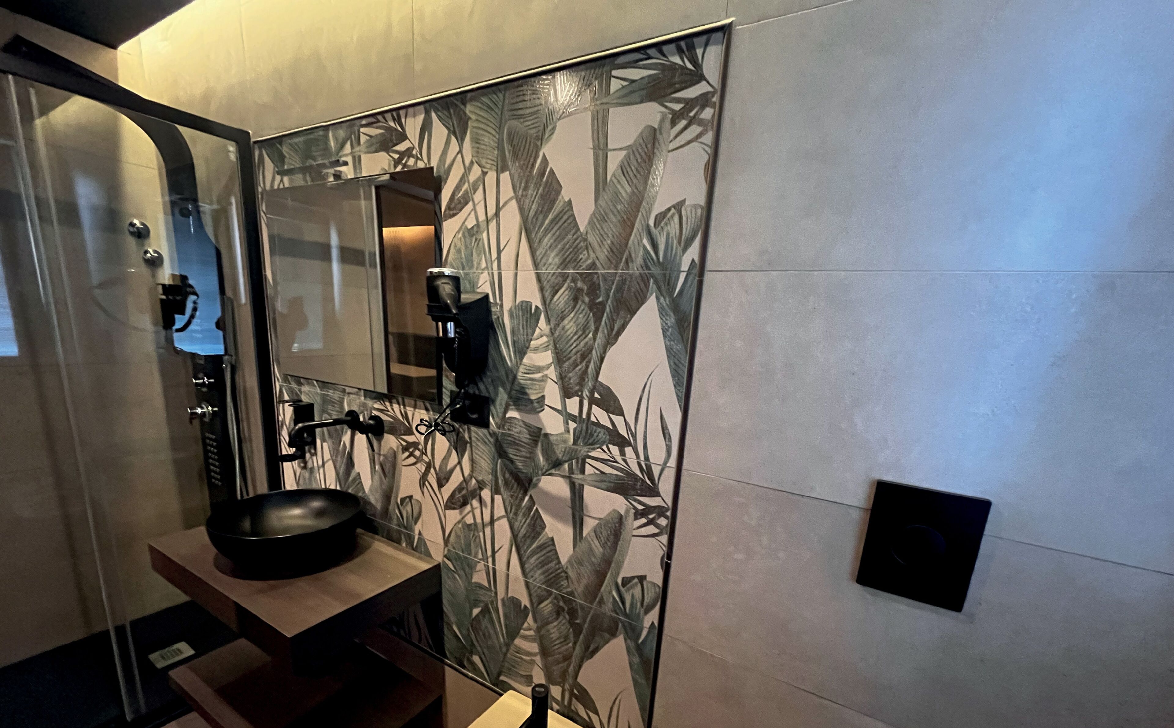 Une salle de bain moderne avec un grand miroir, un lavabo noir et un espace douche.