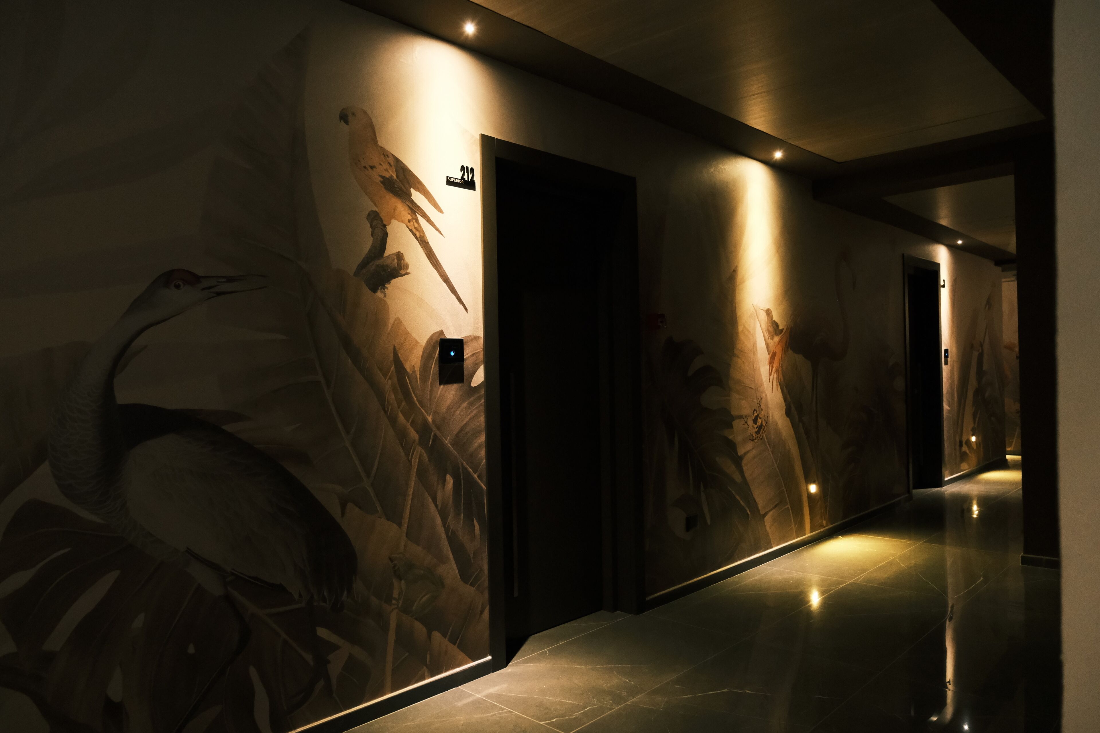 A hallway with a large mural of birds and foliage, a door labeled "212", and a modern, well-lit interior.