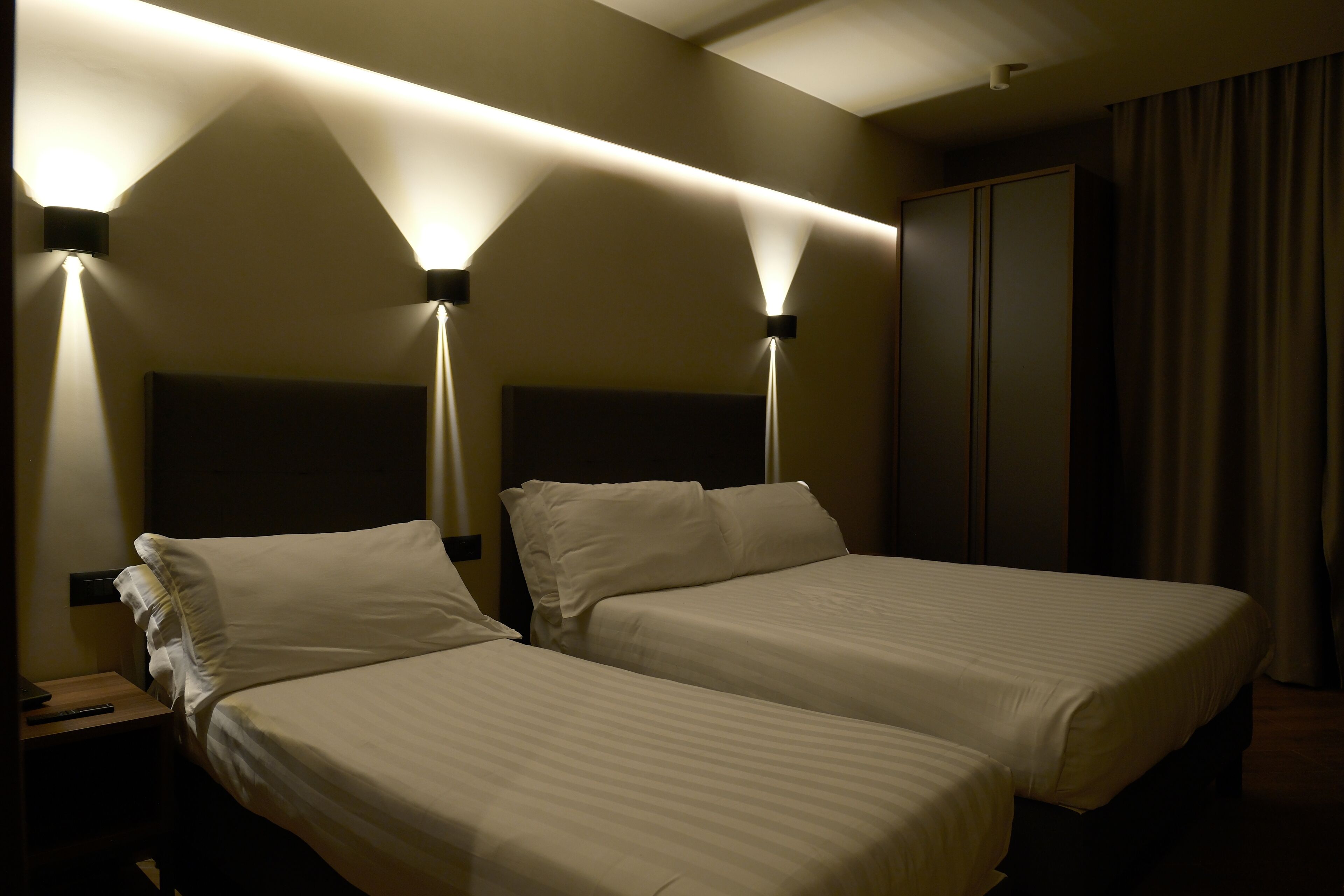 A hotel room with two beds, a nightstand, and a wardrobe.