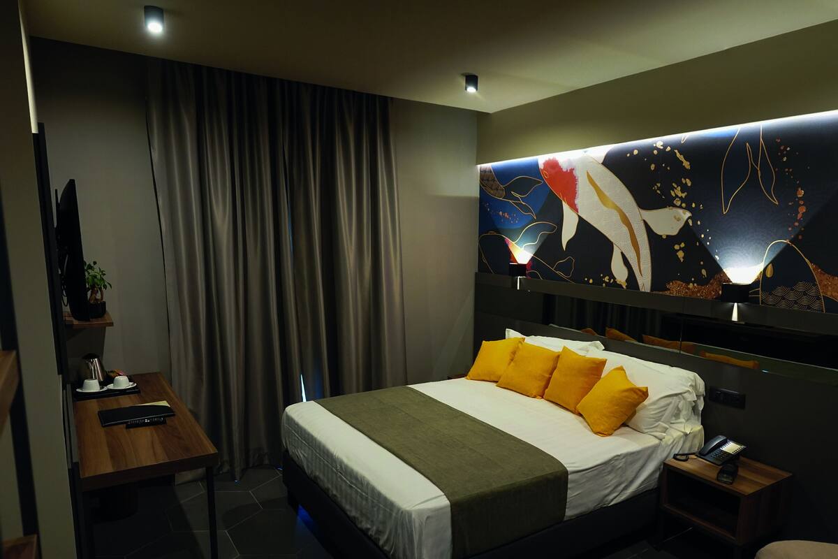 A modern hotel room with a bed, a desk, a chair, a telephone, and a wall-mounted artwork.