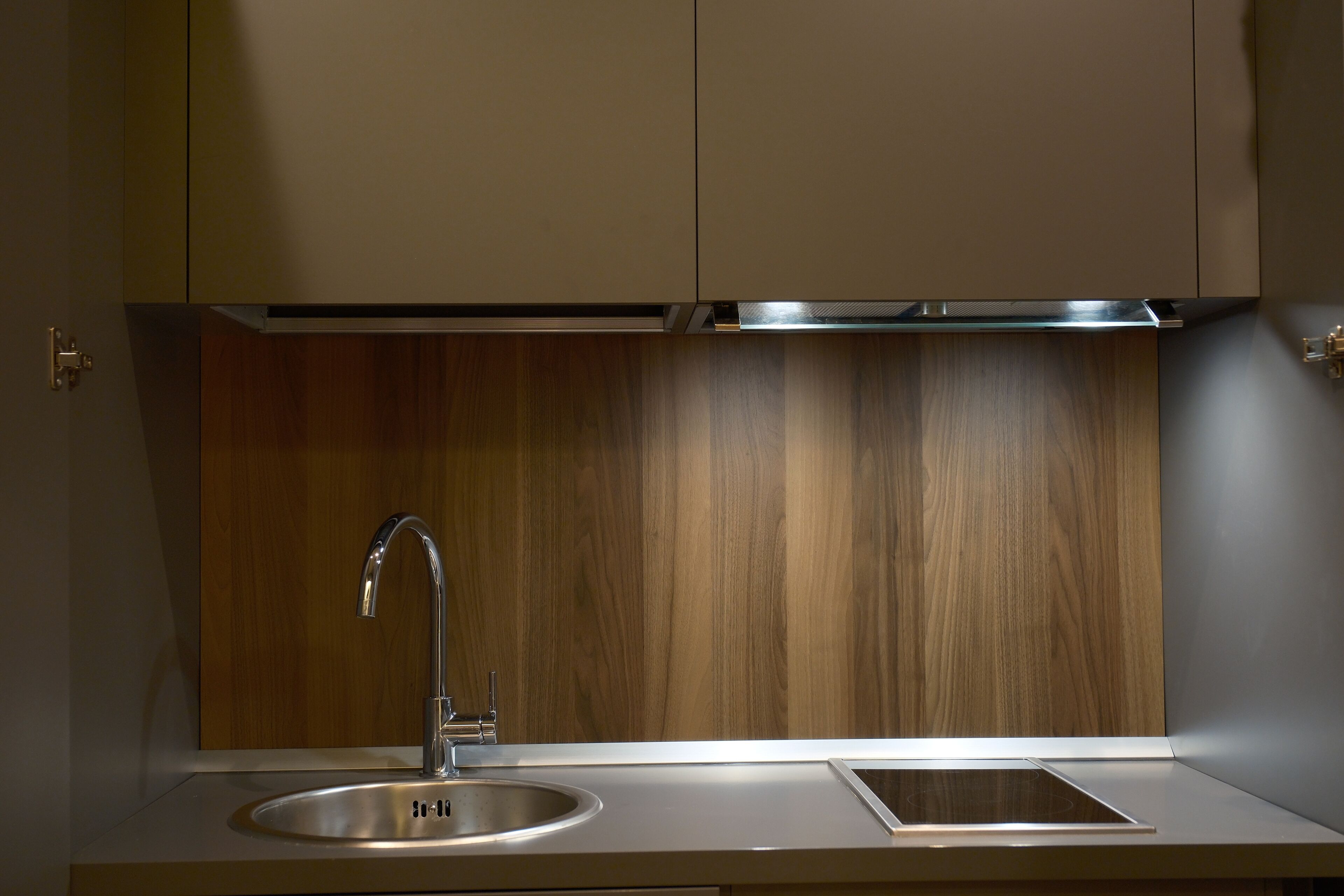 Una cocina moderna con un lavamanos de acero inoxidable, un panel de madera como protector de la pared y luces integradas.
