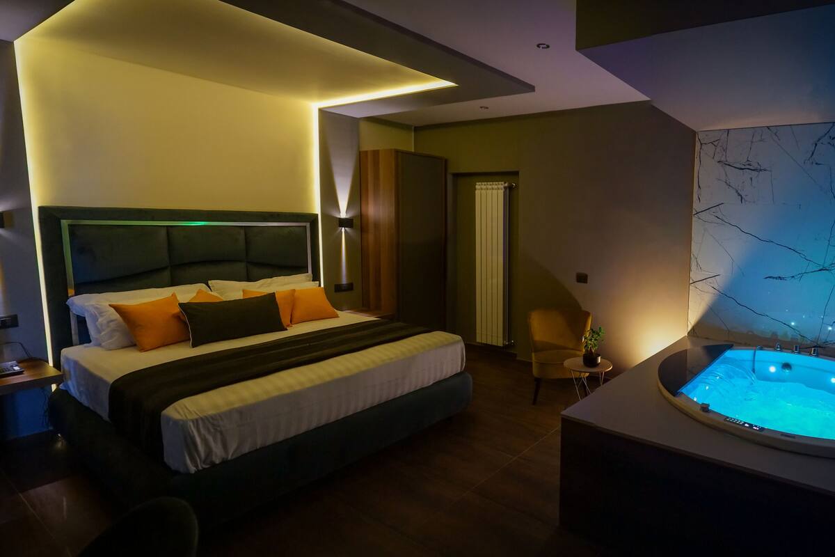 A modern hotel room with a large bed, a small seating area, and a hot tub.