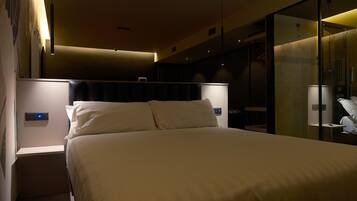 Ein modernes Hotelzimmer mit einem großen Bett, Nachttischen, einer Glasdusche und stimmungsvoller Beleuchtung.