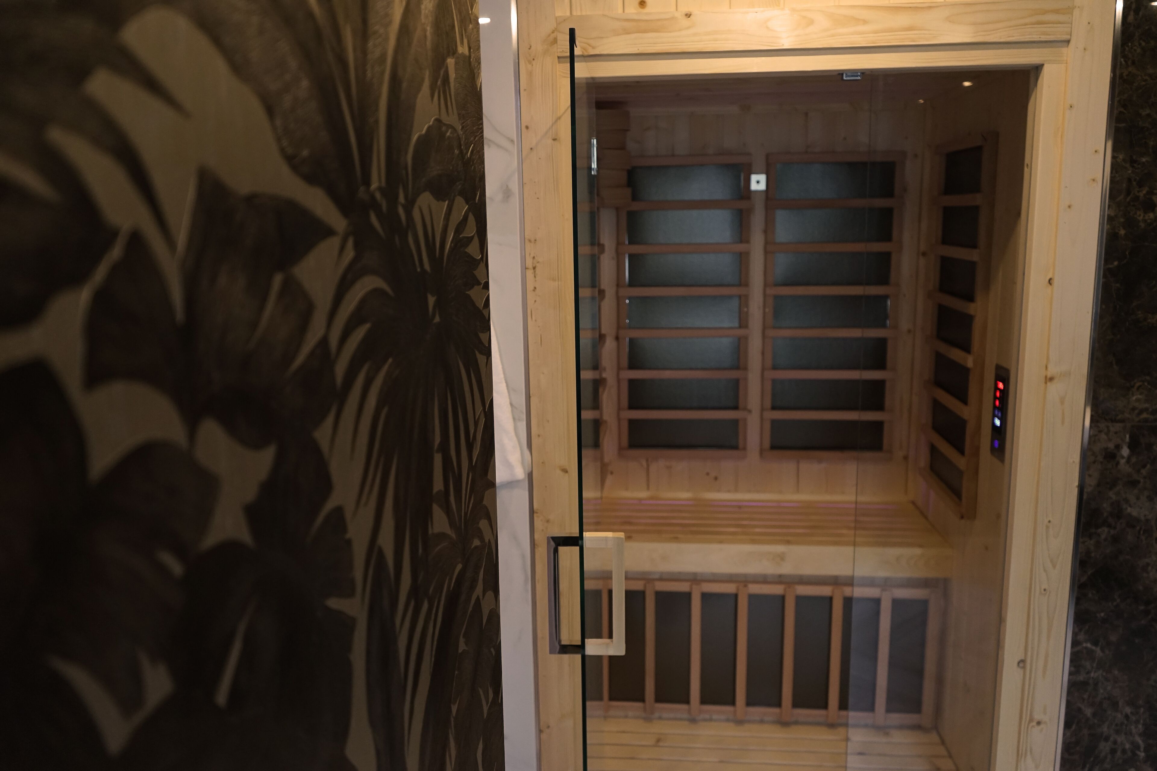 Een sauna met houten wanden en een glazen deur, met een bank en bedieningspaneel.