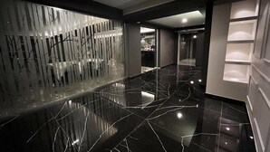 A modern hotel lobby with a reflective black marble floor, a decorative wall with vertical elements, and a glass partition.