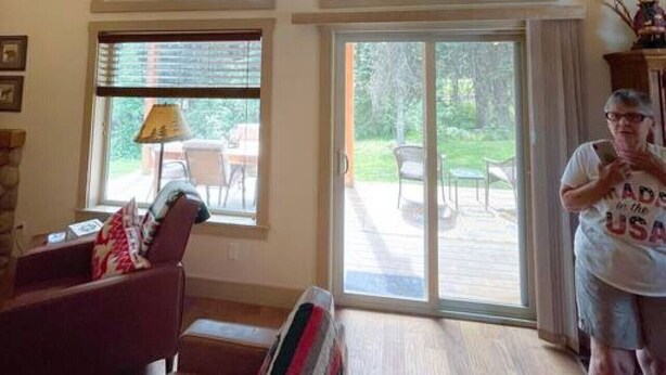 A room with a high ceiling, large windows, a sliding glass door leading to an outdoor area, and a person standing near the door. - Private Cabin at the Foot of the Mountains (Donnelly)
