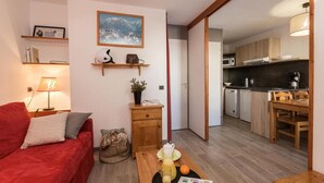 A compact living space with a sofa, a coffee table with drinks, a kitchen area, and a dining table.