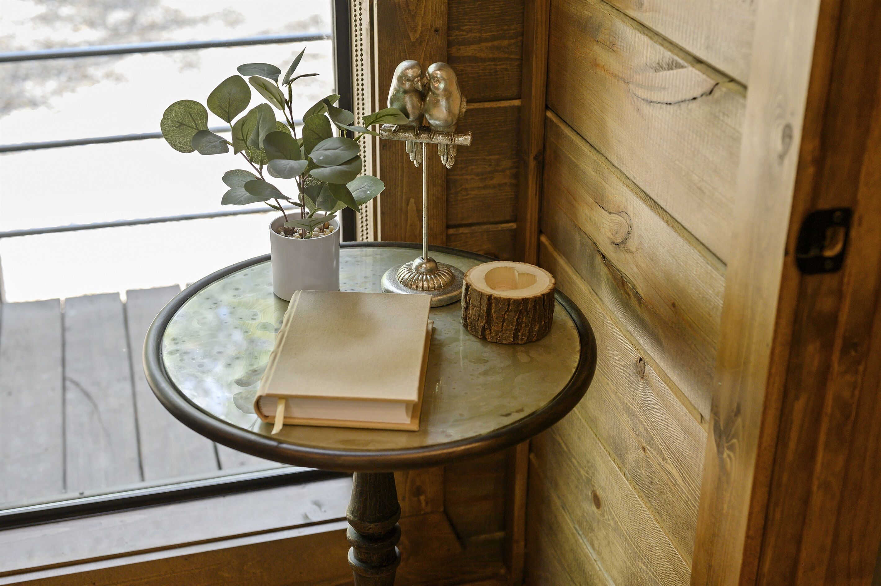 Una pequeña mesa redonda con un libro, una planta en maceta y una escultura de pájaro de madera.