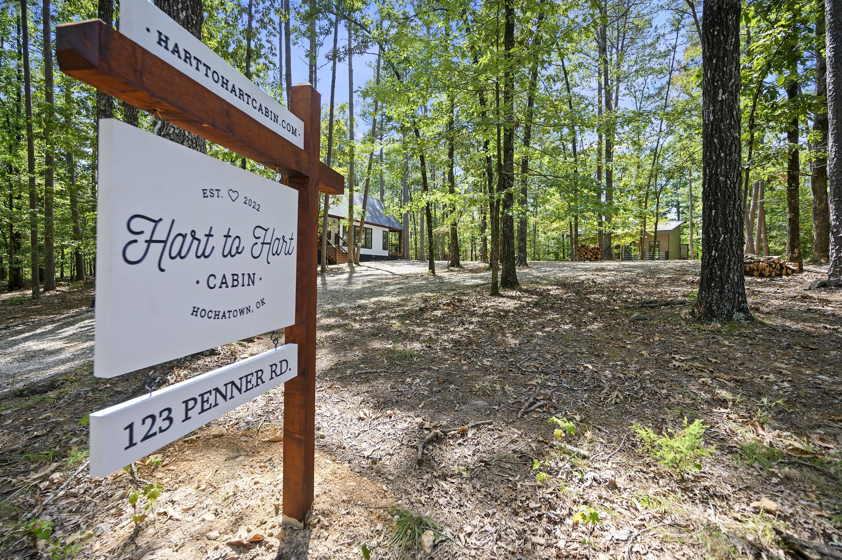 Un letrero de cabaña con la inscripción 'Hart to Hart Cabin' y '123 Penner Rd.' en una zona boscosa.